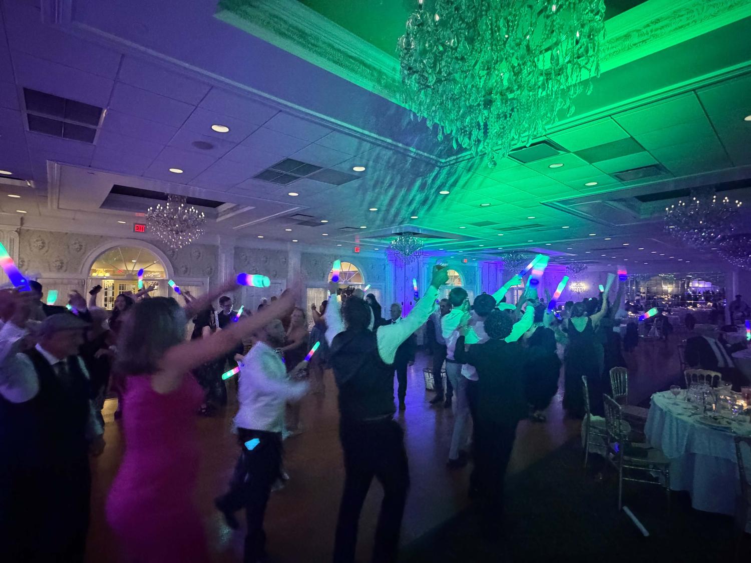 Packed ballroom dance floor with glow sticks under green and purple uplighting