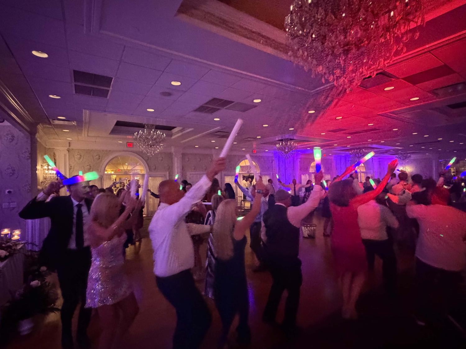 Wedding guests dancing with light-up foam sticks under red and purple lighting